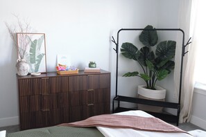 Un dormitorio con cama, cómoda, planta y una obra enmarcada en la pared.