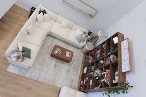 Una sala de estar con un sofá seccional blanco, una mesa de centro de madera y una estantería llena de libros y objetos decorativos.