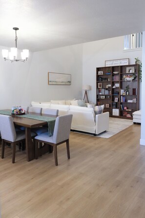A modern living room with a dining area, a white sofa, a bookshelf, and a chandelier. - The Windy Sage - peaceful and family friendly home for any event; sleeps 10+ (Eagle Mountain)