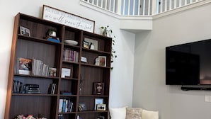 A living room with a bookshelf, a sofa, a coffee table, and a TV mounted on the wall. - The Windy Sage - peaceful and family friendly home for any event; sleeps 10+ (Eagle Mountain)