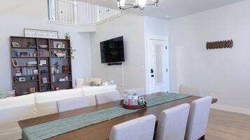 A dining area with a wooden table, chairs, a television mounted on the wall, and a bookshelf filled with books and decorative items.
