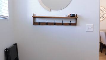 Quarto com um espelho circular fixado na parede, prateleira de madeira com ganchos e um banco de cor escura.