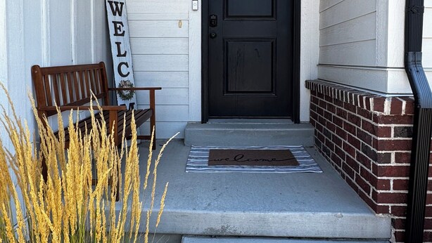 A front porch with a black door, a bench, a welcome mat, and a sign. - The Windy Sage - peaceful and family friendly home for any event; sleeps 10+ (Eagle Mountain)