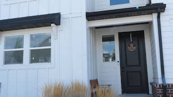 A two-story house with a front door, a small porch, and a window with a light fixture.
