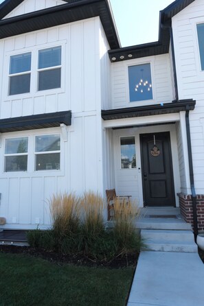 A two-story house with a front door, a small porch, and a window with a light fixture. - The Windy Sage - peaceful and family friendly home for any event; sleeps 10+ (Eagle Mountain)