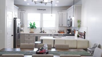 A modern kitchen with white cabinets, a central island, and a dining area with four chairs.