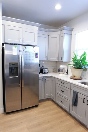 A modern kitchen with white cabinets, a stainless steel refrigerator, a built-in water dispenser, a toaster, and a potted plant. - The Windy Sage - peaceful and family friendly home for any event; sleeps 10+ (Eagle Mountain)