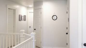 A hallway with white walls, a carpeted floor, and a white railing. There are doors on both sides, and a small round clock on the wall.