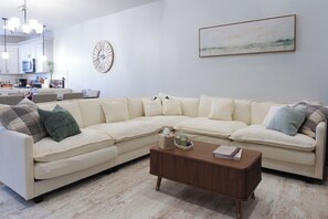 A living room with a sectional sofa, a wooden coffee table, a wall clock, and a framed picture.