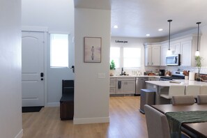 A modern kitchen with white cabinets, a dining area with a table and chairs, and a hallway leading to a door.