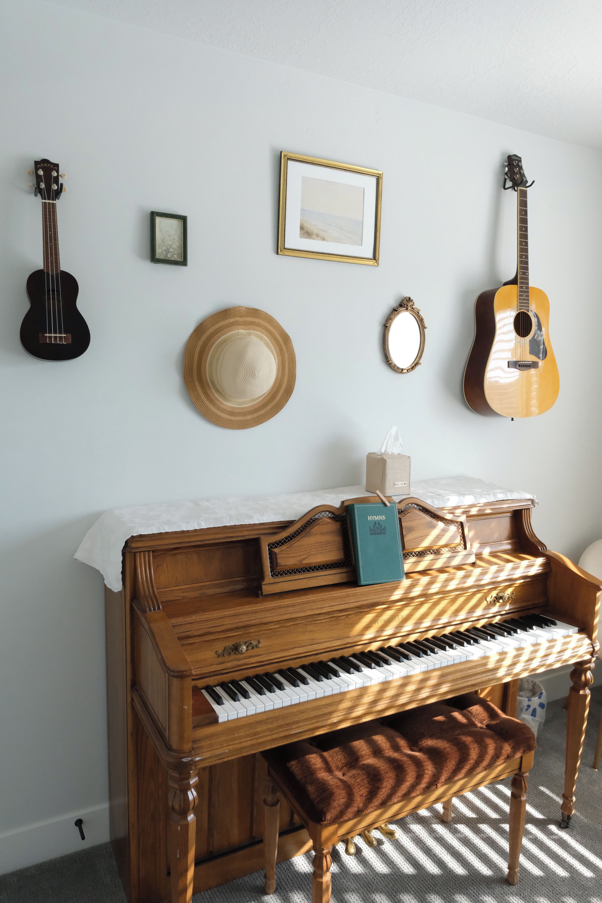 Ein Klavier mit Noten, eine Gitarre, ein gerahmtes Bild, ein Hut und ein Spiegel an der Wand.