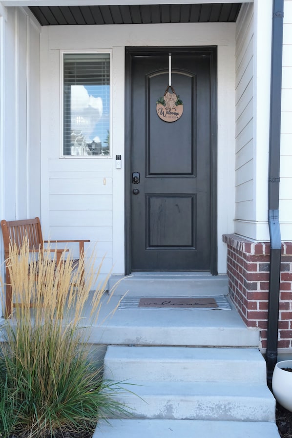 A dark grey front door with a welcome sign, a wooden bench, and a small step leading to the entrance.