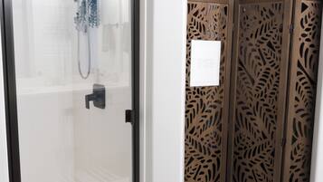A glass-enclosed shower area with a handheld showerhead and a wall-mounted faucet.