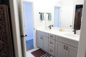 A bathroom with a white vanity, a double sink, and a large mirror. There are two towels hanging on towel bars.