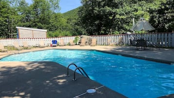 En swimmingpool med ett trästaket, solstolar och ett överbyggt område.