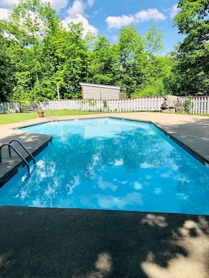 A rectangular swimming pool with a ladder on one side, surrounded by a white fence and trees. - King Bed Studio | Indoor Pool & Hot Tub | Walk to Dining | Minutes to Loon (Lincoln)