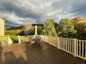 A wooden deck with a white railing, a table with chairs, and a patio umbrella. - King Bed Studio | Indoor Pool & Hot Tub | Walk to Dining | Minutes to Loon (Lincoln)