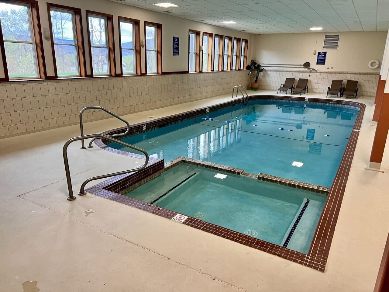 Ein Pool mit Fliesenbelag, einem Rettungsschwimmerstand und Blick ins Freie durch große Fenster.