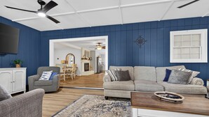 A living room with a sofa, armchair, and a coffee table. There is a fireplace, a ceiling fan, and a television mounted on the wall. - Sandy Shores Pool & Spa Retreat w/Hot Tub/Beach (Summerton)
