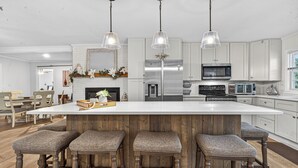 A modern kitchen with a large island, bar stools, stainless steel appliances, and pendant lighting. - Sandy Shores Pool & Spa Retreat w/Hot Tub/Beach (Summerton)