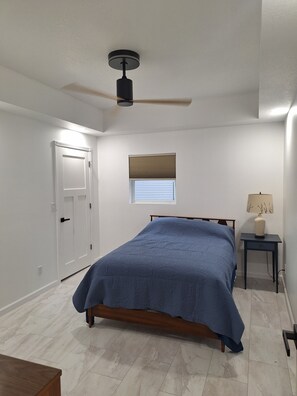 A bedroom with a bed, a ceiling fan, a window with blinds, a bedside table, and a door. - 3-bedroom house in soothing Manistique with plenty of space to relax (Manistique)