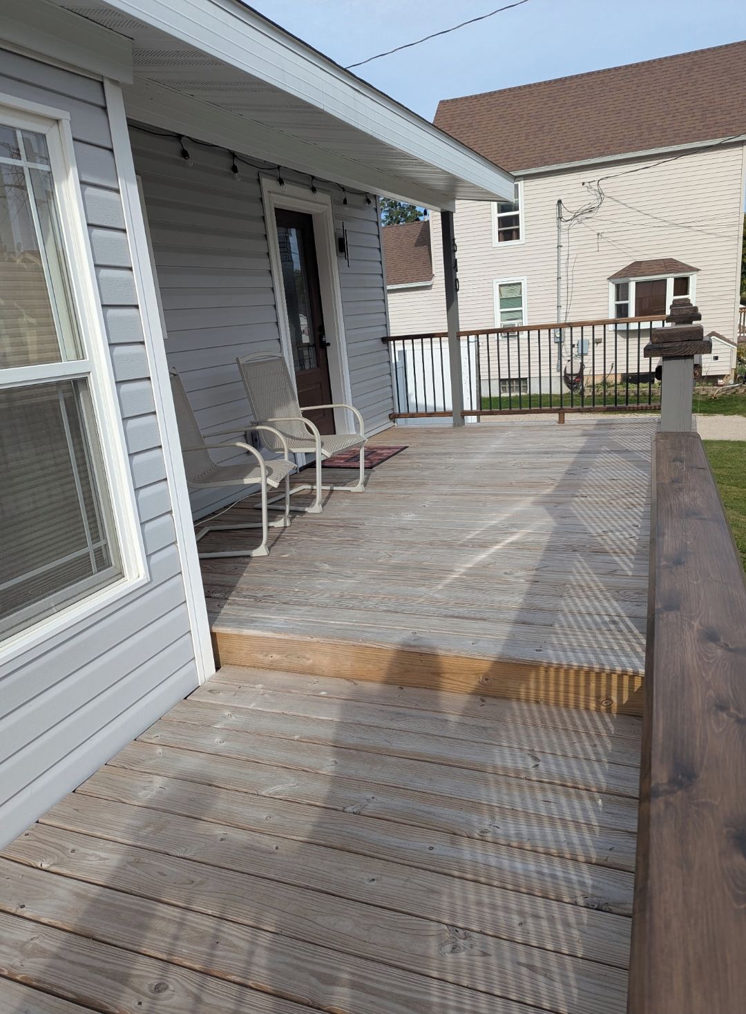 Una terraza de madera con un porche cubierto, una silla blanca y una mesita.