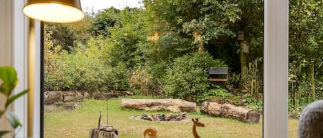 A window with a view of a garden featuring a deer, a fox, and a bird feeder.