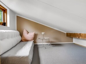 Quarto moderno e minimalista com sofá branco, mesa redonda pequena e teto inclinado.