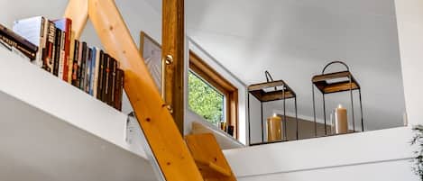 Una escalera de madera lleva a una zona superior con estanterías y dos faroles fijados a la pared.