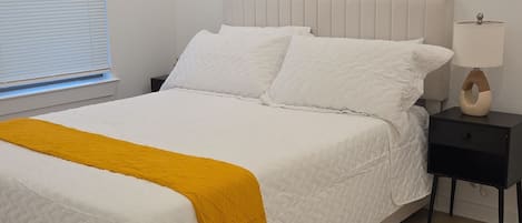 Une chambre à coucher avec un lit, une table de chevet, une lampe et une fenêtre avec des stores.