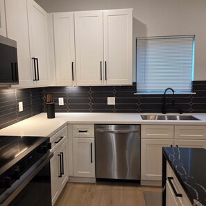 A modern kitchen with white cabinets, black backsplash, stainless steel appliances, and a window with blinds. - Modern Retreat / Near Downtown• NRG • Med Ctr (Houston)