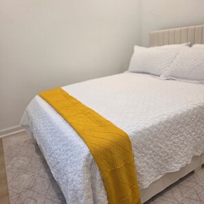 Ein Bett mit weißer Bettdecke und gelbener Tagesdecke.