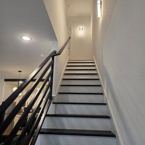 A staircase with black handrails and white walls, leading to a room with a cross on the wall. - Modern Retreat / Near Downtown• NRG • Med Ctr (Houston)