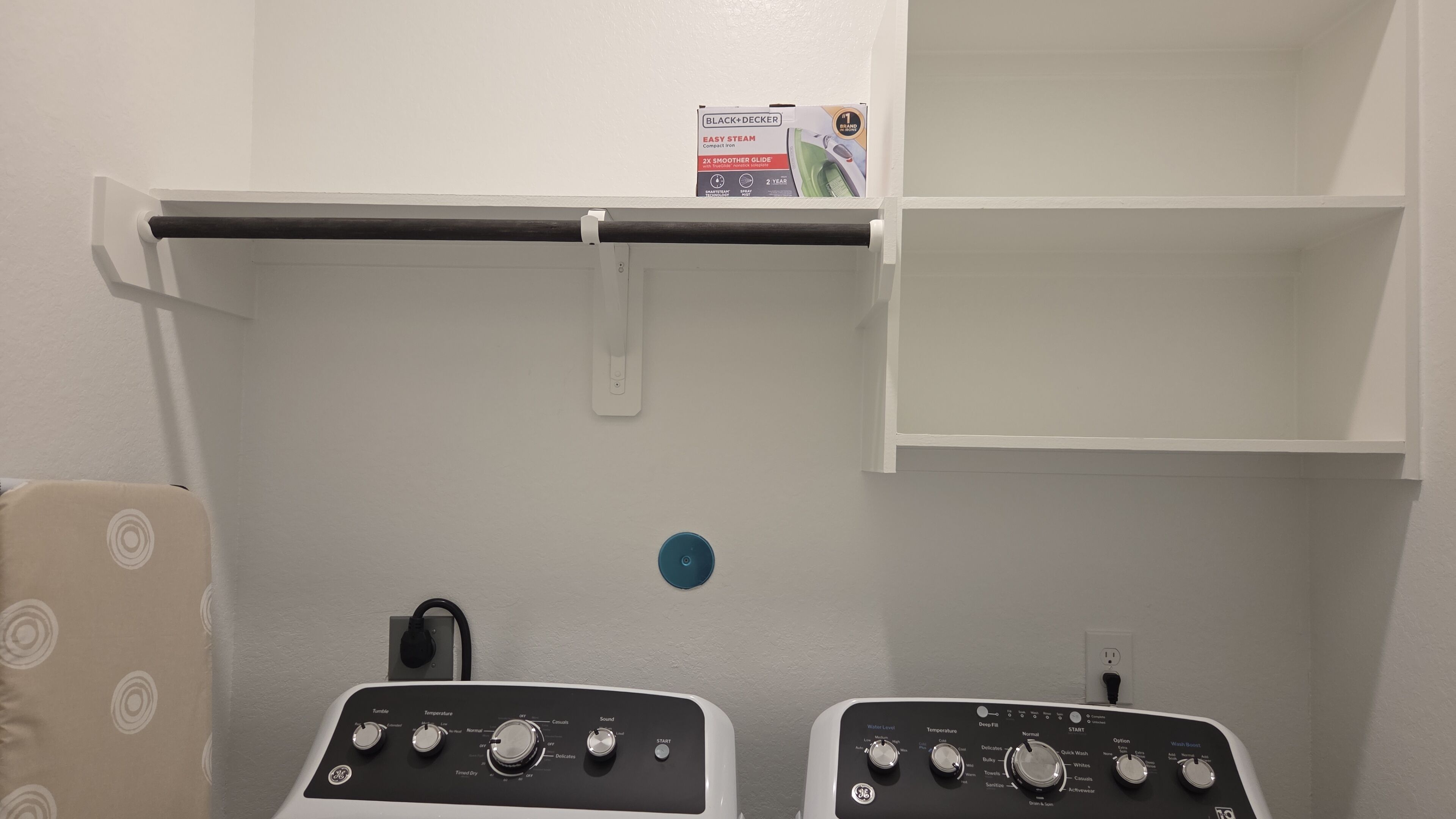 A compact iron with a control panel, a power outlet, and a wall-mounted shelf with a box.