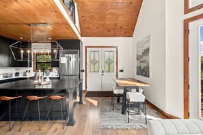 A modern kitchen with a central island, stainless steel appliances, and a dining area with a wooden table and chairs. - Edgewood Retreat – Modern Luxury Cabin in Chalet Village (Gatlinburg)