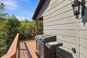 A wooden deck with a barbecue grill and a wall-mounted lantern. - Edgewood Retreat – Modern Luxury Cabin in Chalet Village (Gatlinburg)