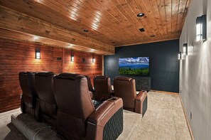 Ein Heimkino mit Holzvertäfelung, Ledersesseln, einem großen Flachbildfernseher und Teppichboden.