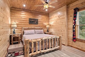 A wooden cabin bedroom with a bed, two nightstands, a ceiling fan, and a window with curtains. - Chestnut Tower – Incredible Mount LeConte Views, Hot Tub & Game Room (Gatlinburg)