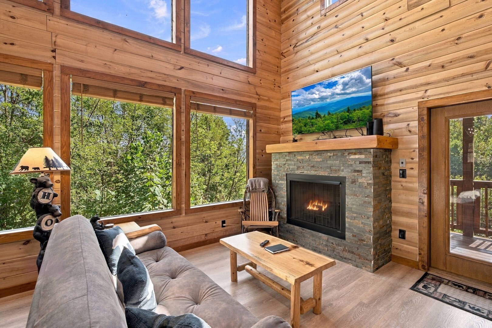 A log cabin interior with a fireplace, large windows, and a sofa.