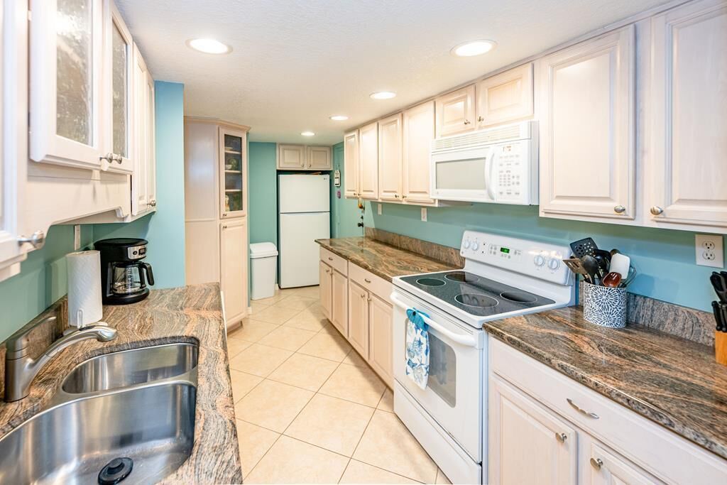 A kitchen with white cabinets, a stove, a microwave, and a sink.