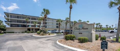 A multi-story hotel with a sign reading 'Ocean House 7870' and a parking lot with several cars.