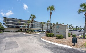 Ein mehrgeschossiges Hotel mit einem Schild, auf dem 'Ocean House 7870' steht, und einem Parkplatz mit mehreren Autos.