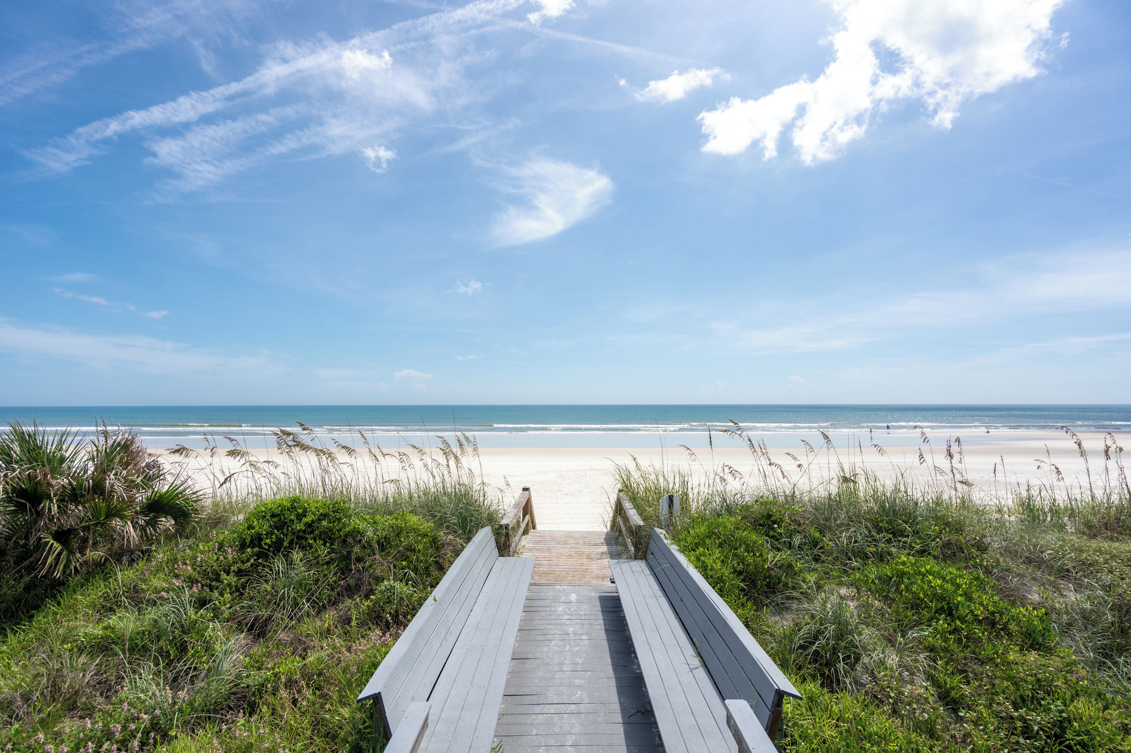A wooden boardwalk leading to a beach with a clear sky.