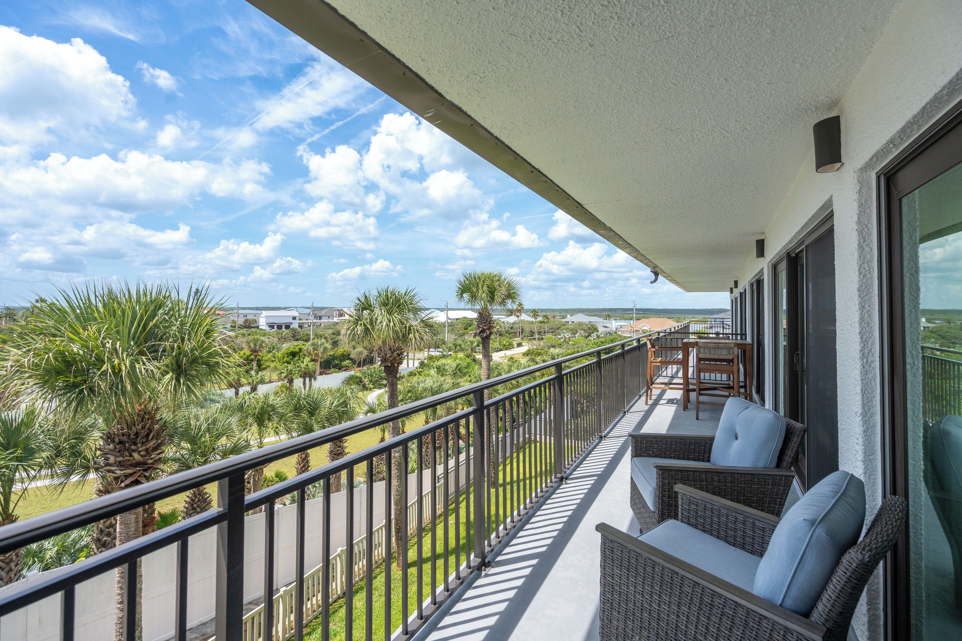 A balcony with wicker furniture, a white railing, and a view of a green landscape with palm trees.