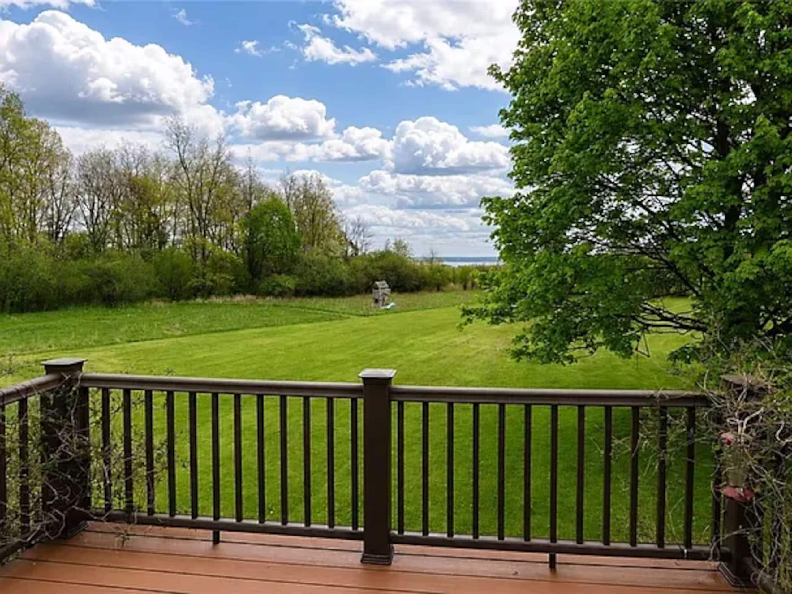 A wooden deck with a railing overlooking a well-maintained lawn and trees.