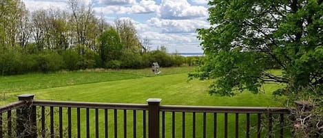 A wooden deck with a railing overlooking a well-maintained lawn and trees.