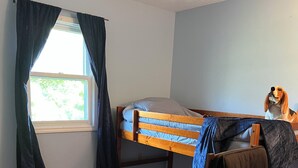 Quarto com beliche, escrivaninha, cadeira e janela com cortinas.