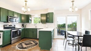 Cozinha moderna com armários verdes, uma ilha central e uma área de jantar com mesa e cadeiras.