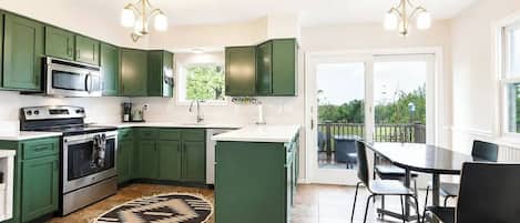 A modern kitchen with green cabinets, a central island, and a dining area with a table and chairs.