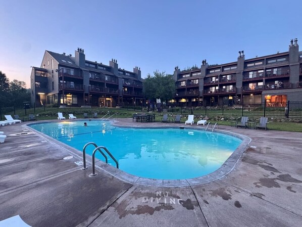 Una piscina con sillones de descanso y un edificio con balcones al fondo.